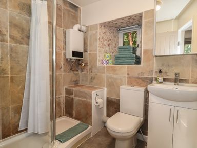 A bathroom with a shower area with a curtain a toilet a sink with cabinet and a small window with towels at Pear Tree Lodge in Combe near Langport