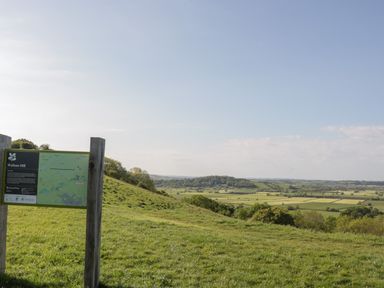 A grassy hillside with a Walton Hill National Trust sign and a view of fields and trees at Pear Tree Lodge in Combe near Langport