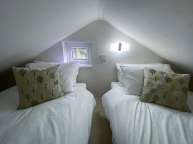 A small attic bedroom with two single beds each with white bedding and tree patterned cushions at Pear Tree Lodge in Combe near Langport