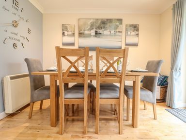A dining room with a wooden table and six chairs with paintings on wall and clock at Manuka in Falmouth