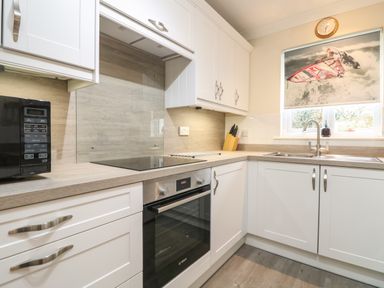 A kitchen with white cabinets a built-in oven a microwave a sink and a window with a windsurfing blind at Manuka in Falmouth