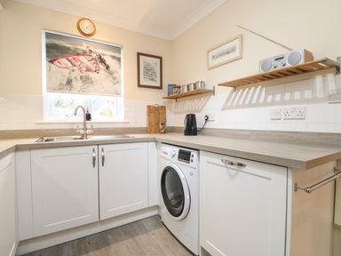 A kitchen with white cabinets a washing machine a sink and shelves with a radio and containers at Manuka in Falmouth