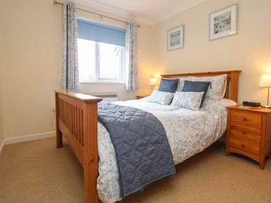 A bedroom with a wooden bed and bedside tables with lamps and framed pictures on walls at Manuka in Falmouth