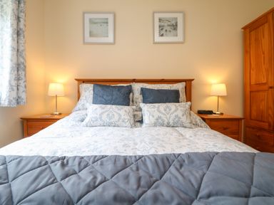 A bedroom with a wooden bed frame blue and white patterned bedding two bedside tables with lamps and a wooden wardrobe at Manuka in Falmouth