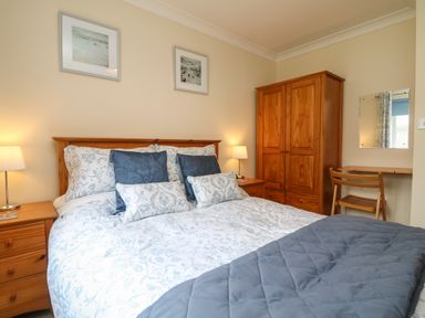 A bedroom with a double bed blue and white bedding two bedside tables with lamps wooden wardrobe desk and chair at Manuka in Falmouth