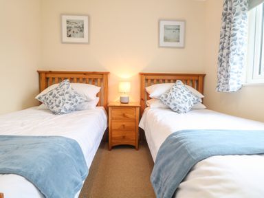 A bedroom with two single beds a wooden nightstand and a lamp at Manuka in Falmouth