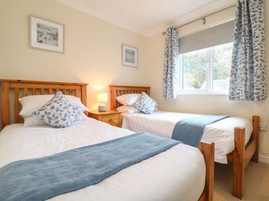 A bedroom with two single wooden beds a nightstand in between a lamp two framed pictures and a window with curtains at Manuka in Falmouth