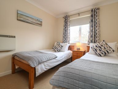 A bedroom with two single beds a nightstand with a lamp and geometric patterned curtains at Manuka in Falmouth