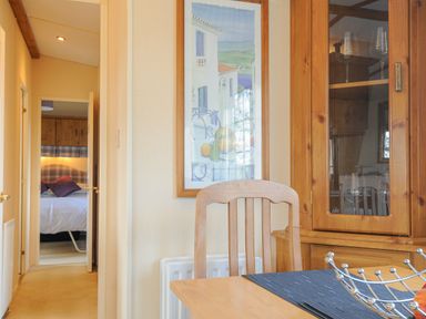 A dining room with a wooden chair a cabinet with glass doors and a framed painting with a view into a bedroom with a bed at Little Malory in St Giles-On-The-Heath