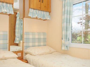 A bedroom with two single beds with star patterned bedding a window with curtains and wooden cabinets above the beds at Little Malory in St Giles-On-The-Heath