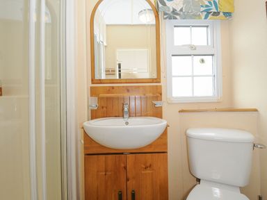 A bathroom with a sink, wooden cabinet, mirror, window, and toilet at Little Malory in St Giles-On-The-Heath