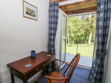 A small room with a wooden desk and chair next to an open door with curtains leading to a garden view at Glanduad Fawr in Newport Pembrokeshire