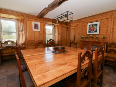 A dining room with a large wooden table and chairs wood panelled walls and framed pictures at Glanduad Fawr in Newport Pembrokeshire