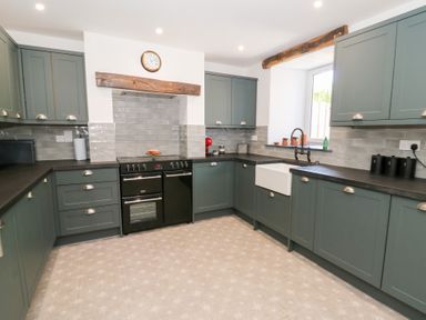 A kitchen with green cabinets a black oven a farmhouse sink and a clock on the wall at Glanduad Fawr in Newport Pembrokeshire
