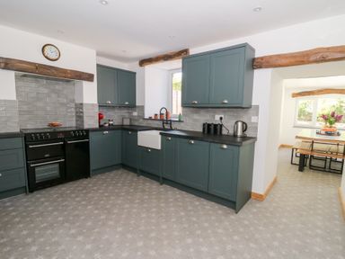 A kitchen with green cabinets a black stove a white farmhouse sink and a dining area visible through an archway at Glanduad Fawr in Newport Pembrokeshire