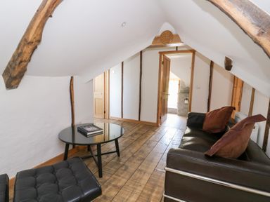 A small sitting area with a black sofa, cushions, a glass coffee table, and wooden floorboards at Glanduad Fawr in Newport Pembrokeshire