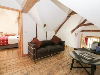A sitting area with black leather sofas brown cushions and a glass coffee table next to a bedroom with a red blanket at Glanduad Fawr in Newport Pembrokeshire
