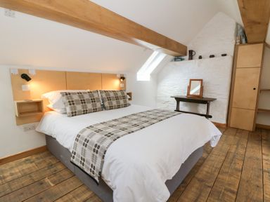 A bedroom with a bed wooden floor a small table with a mirror and built in wooden shelves at Glanduad Fawr in Newport Pembrokeshire
