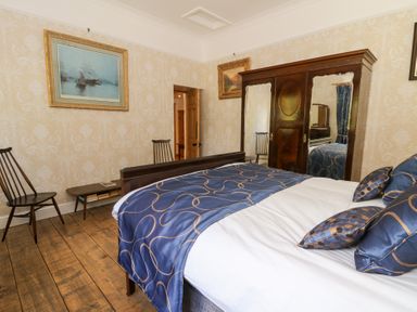 A bedroom with a wooden bed blue bedding wooden wardrobe with mirrors chairs and paintings at Glanduad Fawr in Newport Pembrokeshire