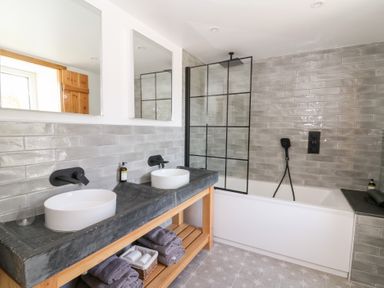 A bathroom with double sinks and countertop next to a bathtub with a black framed shower screen at Glanduad Fawr in Newport Pembrokeshire