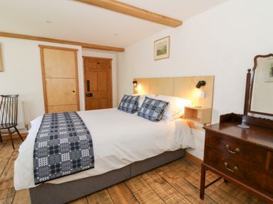 A bedroom with a bed with patterned pillows and runner a wooden chest of drawers and a chair at Glanduad Fawr in Newport Pembrokeshire
