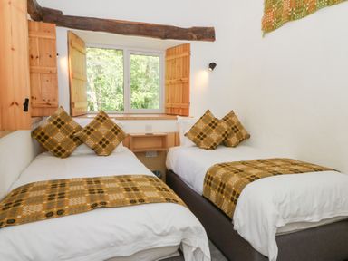 A bedroom with two single beds with patterned cushions and throws near a window at Glanduad Fawr in Newport Pembrokeshire