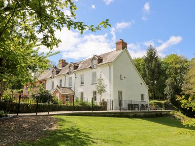 A white two-story house with chimneys and a fenced patio area surrounded by trees and grass at Glanduad Fawr in Newport Pembrokeshire