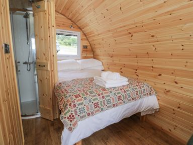 A bedroom with a double bed towels on bed wooden walls and a shower cubicle at Tarrenhendre Pod in Llanegryn near Tywyn