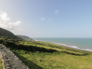A coastal landscape with grassy fields, stone walls, hillside, and the sea at Tarrenhendre Pod in Llanegryn near Tywyn
