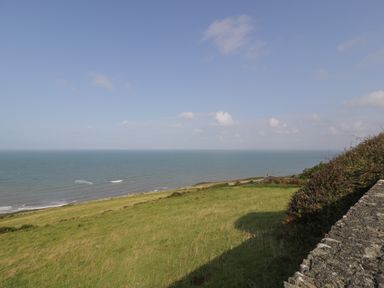 A grassy hillside overlooking the sea with a stone wall and some bushes at Tarrenhendre Pod in Llanegryn near Tywyn