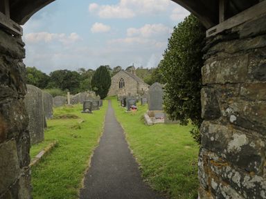 A pathway through a graveyard with gravestones and a stone church at the end at Tarrenhendre Pod Llanegryn near Tywyn