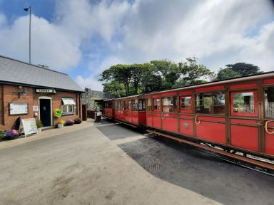 A red train at a small station platform with a brick building labeled ladies and gentlemen nearby at Tarrenhendre Pod in Llanegryn near Tywyn