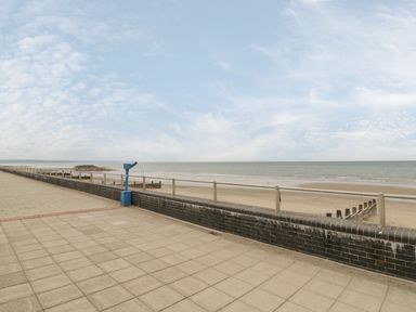 A paved promenade with a blue viewing telescope and railing overlooking a sandy beach and the sea at Tarrenhendre Pod in Llanegryn near Tywyn