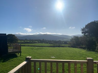 A grassy lawn with wooden railing and a pod structure overlooking hills under a clear sky at Tarrenhendre Pod in Llanegryn near Tywyn