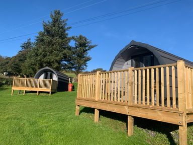 Two small cabins with wooden decks on green grass near trees at Tarrenhendre Pod in Llanegryn near Tywyn
