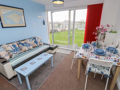 A living room with sofa table and dining table near large glass doors with a view outside at Culver View in Sandown