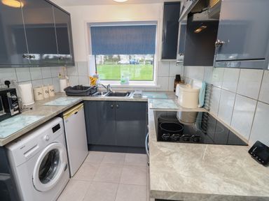 A kitchen with grey cabinets a washing machine a refrigerator a sink and an electric stove at Culver View in Sandown