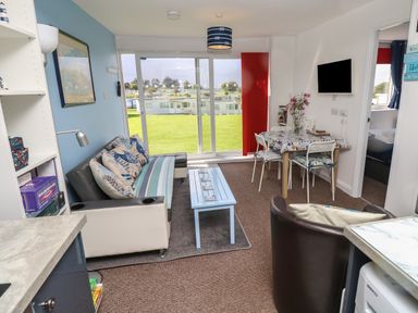 A living room with a sofa and cushions a coffee table a dining table with chairs and flowers mounted tv and sliding glass doors with a view at Culver View in Sandown