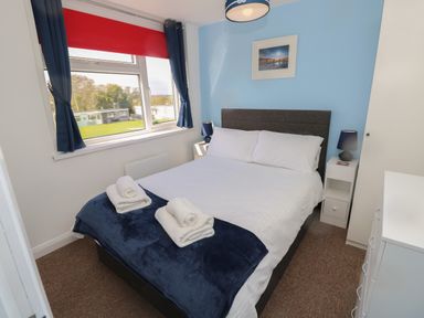 A bedroom with a double bed white and blue bedding bedside tables lamps a window with curtains and a wardrobe at Culver View in Sandown