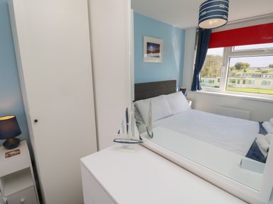 A bedroom with a bed next to a window a blue lamp on a bedside table and a white wardrobe at Culver View in Sandown