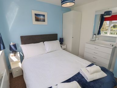 A bedroom with a double bed bedside tables lamps wardrobe and a chest of drawers with a mirror at Culver View in Sandown