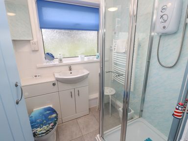 A bathroom with a sink cabinet shower enclosure and toilet with ocean themed seat cover at Culver View in Sandown