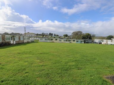 A grass field surrounded by single-story buildings under a partly cloudy sky at Culver View in Sandown
