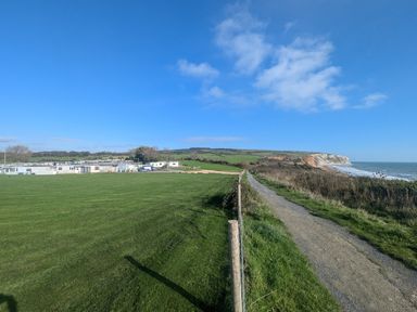 A coastal path next to a grassy field with caravans and a cliff by the sea at Culver View in Sandown