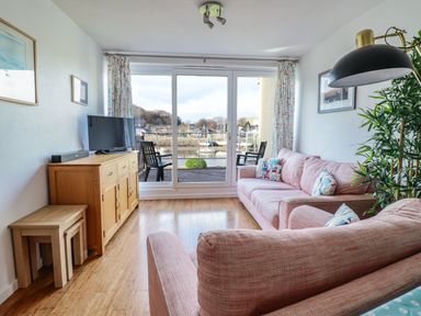 A living room with pink sofas facing a wooden cabinet with a tv and glass doors at Branwen in Porthmadog