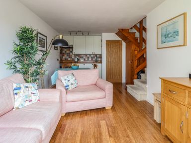 A living room with pink sofas and pillows a wooden floor a kitchen area with cabinets and a dining table and wooden stairs at Branwen in Porthmadog