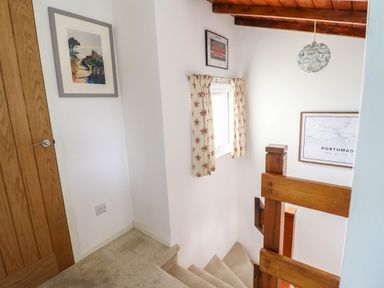 A staircase with wooden railing a window with patterned curtains and framed pictures on white walls at Branwen in Porthmadog