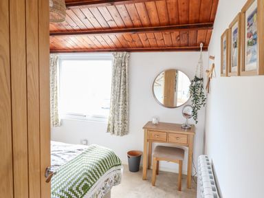 A bedroom with a wooden dressing table a round mirror a stool and a bed with a green and white blanket at Branwen in Porthmadog