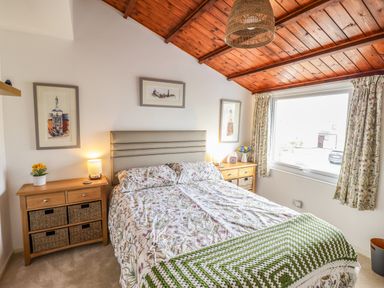 A bedroom with a double bed wooden ceiling two bedside tables with lamps and a window with curtains at Branwen in Porthmadog