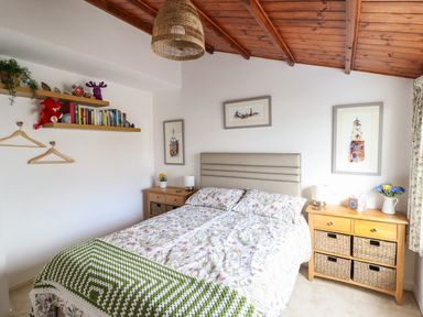 A bedroom with a bed two wooden bedside tables a wooden ceiling and shelves with books and toys at Branwen in Porthmadog